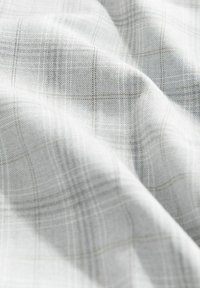 Tessuto testurizzato di un grigio chiaro con un leggero motivo a scacchi. Il materiale presenta una morbida texture intrecciata e un sottile lucido.