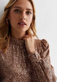 Bronze sequin top with high neck, puffed sleeves, and button accents on cuff. Smooth texture with shimmering details throughout.