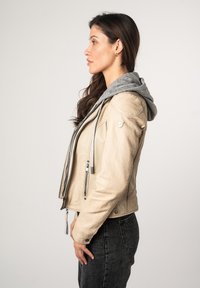 Beige leren jack met een grijze hoodie. Bevat ritsen en textuurdetails. Ontworpen met een cropped fit en een zijaanzicht profiel.