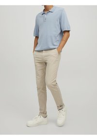 Ljusblå polo skjorta med tre knappar, kombinerad med beige slim-fit byxor och vita sneakers. Enkel design, avslappnad stil.