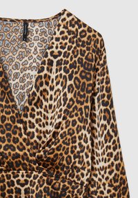 Halenka s leopardím potiskem, navržená ve stylu zavinovací, s dlouhými rukávy a hladkým materiálem. Barvy zahrnují odstíny hnědé, černé a světle modré akcenty.