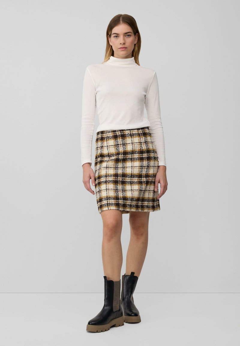 Witte coltrui, geruite minirok in beige, bruin en zwart. Zwarte kniehoge laarzen met dikke zolen. Gladde stof. Casual outfit.