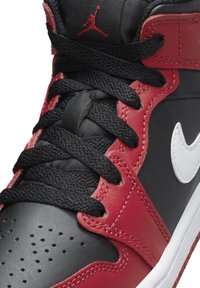 Czarne skórzane sneakersy z czerwonymi akcentami, z białym logo i czarnymi sznurowadłami. Teksturowana powierzchnia i perforowany czubek dla lepszej wentylacji.