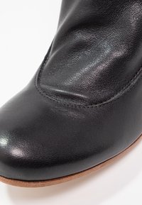 Gros plan sur le bout d'une botte en cuir noir avec couture visible et bord de semelle lisse marron sur fond blanc.