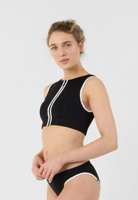 Reggiseno sportivo nero con scollatura alta, rifiniture bianche e zip anteriore. Abbinato a slip da bikini neri con rifiniture bianche simili.
