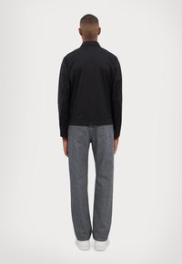 Musthave musta kerge jope krae ja pikkade varrukatega, mis on kombineeritud hallide sirgete pükstega ja valgete sussidega. Lihtne disain, ilma nähtavate mustriteta.