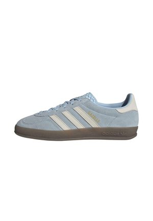 Lichtblauwe suède sneaker met drie witte strepen, ronde neus en platte rubberen zool. Beschikt over gouden branding "Gazelle" en "adidas."