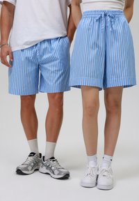 Modré a bílé pruhované šortky s elastickým pasem. Spárováno se sportovními botami. Unisex design; fit a do poloviny stehen.