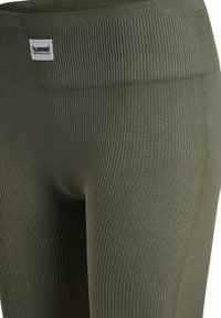 Olivgröna ribbade leggings med en bred midjeband. Har en liten märkesetikett framtill. Mjuk textur, figurnära passform och elastiskt material.