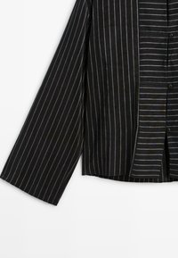Camicia a righe nera e grigia con maniche lunghe, chiusura frontalmente a bottoni, larghezze delle righe variabili e orlo dritto.