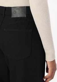 Mustad denim püksid sisaldavad tagataskut ja tekstuuriga musta nahkpatchi. Tekstuuriga patchil on lillemuster.