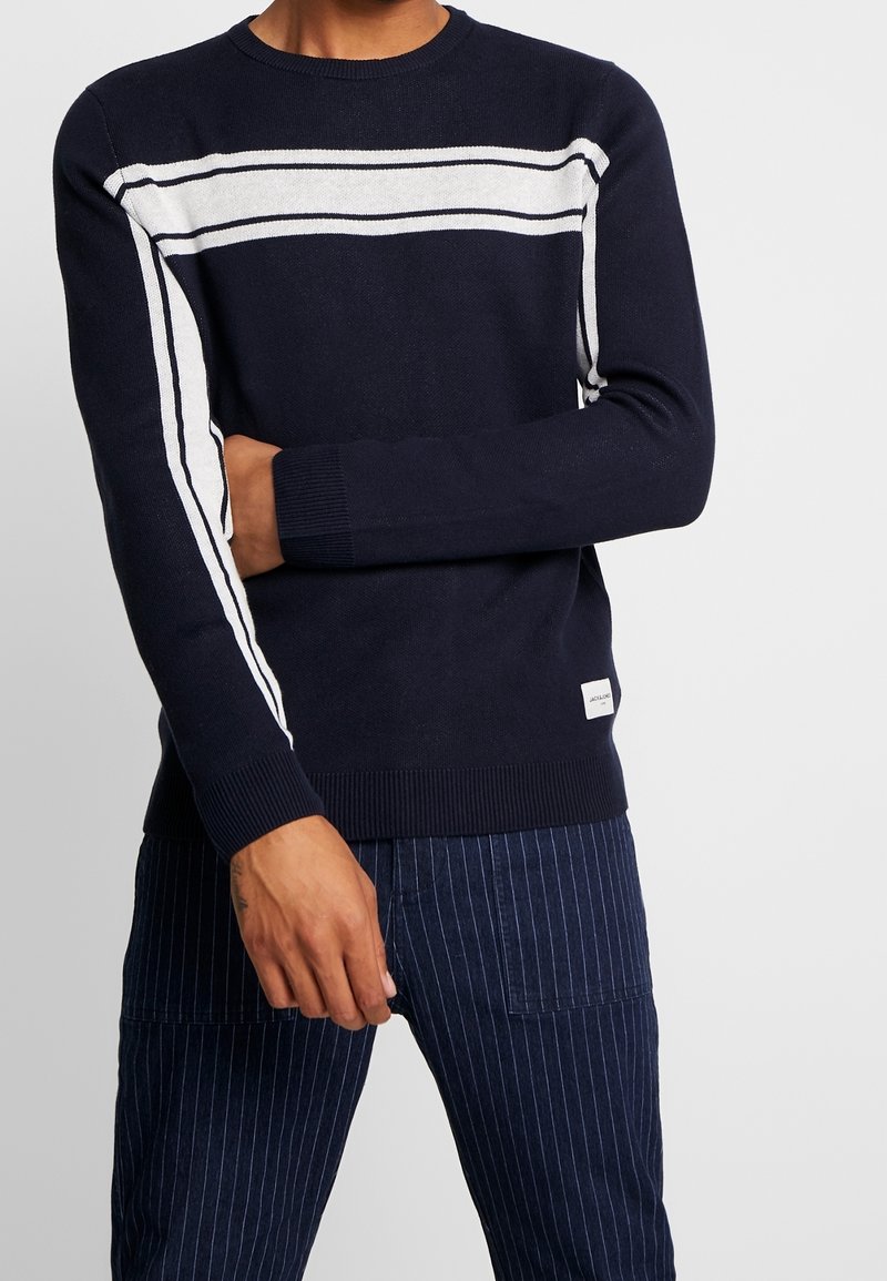 Navy gestrickter Pullover mit weißen Streifen, Rundhalsausschnitt und gerippten Bündchen. Strukturiertes Material und kleines Logoschildchen nahe dem Saum.
