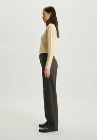Pull en tricot beige, coupe slim, manches longues. Pantalon rayé foncé, taille haute, jambe droite. Mocassins noirs à petit talon.