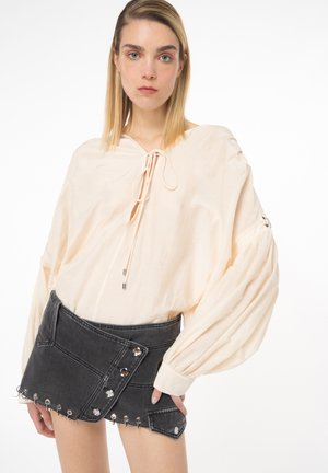 Blusa pesca con scollo a cordoncino e maniche a palloncino, abbinata a una gonna avvolgente in denim nera con bottoni a scatto e dettagli con occhielli.