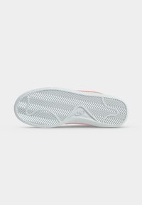 Η σόλα ενός λευκού αθλητικού παπουτσιού Nike με μοτίβο ψαροκόκκαλο και λογότυπο Swoosh, σε προβολή από κάτω με απλό φόντο.