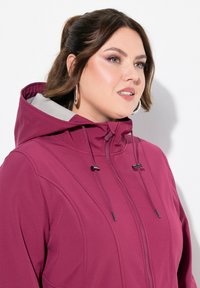 Maroon hooded jacket with a front zipper, drawstring details, and a contrast lined hood. The fabric appears smooth with subtle stitching accents.