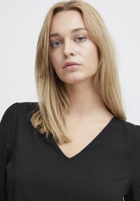 Blusa nera a V con maniche lunghe, realizzata in tessuto morbido. Texture liscia con dettagli minimi, adatta per abbigliamento casual o formale.