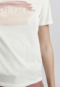 Witte katoenen t-shirt met een roze penseelstrekenontwerp en de tekst "SIMPLE IS BEAUTIFUL." Korte mouwen en ronde hals.