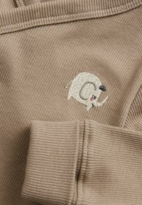 Beige ribbet stof med en broderet elefant iført en sort hat, med synlig syning og en blød tekstur.