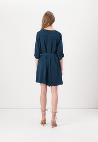 Robe à manches courtes bleu sarcelle foncé avec ceinture, présentant une coupe décontractée, une légère forme trapèze et des manches retroussées, confectionnée dans un tissu léger.