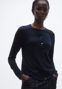 Tmavomodrý prispôsobený sveter na zapínanie s guľatým výstrihom, dlhými rukávmi a zapínaním na gombíky vpredu, vyrobený z mäkkej látky.