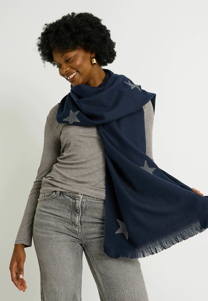 Écharpe marine en tissu doux, ornée d'étoiles argentées et avec des franges aux extrémités, drapée sur les épaules au-dessus d'un haut gris.