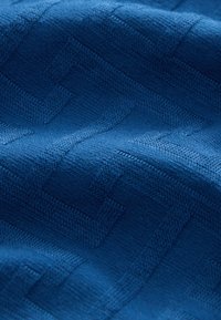 Blauwe gebreide stof met een getextureerd geometrisch patroon. Het materiaal lijkt zacht met zichtbare stiksel details, die diepte en dimensie creëren.