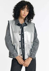 Silberfarbene metallische Weste mit grauen Denim-Ärmeln, Knopfverschluss vorne und zwei Vorderaschen. Sie hat einen Kragen und kontrastierende Kanten.