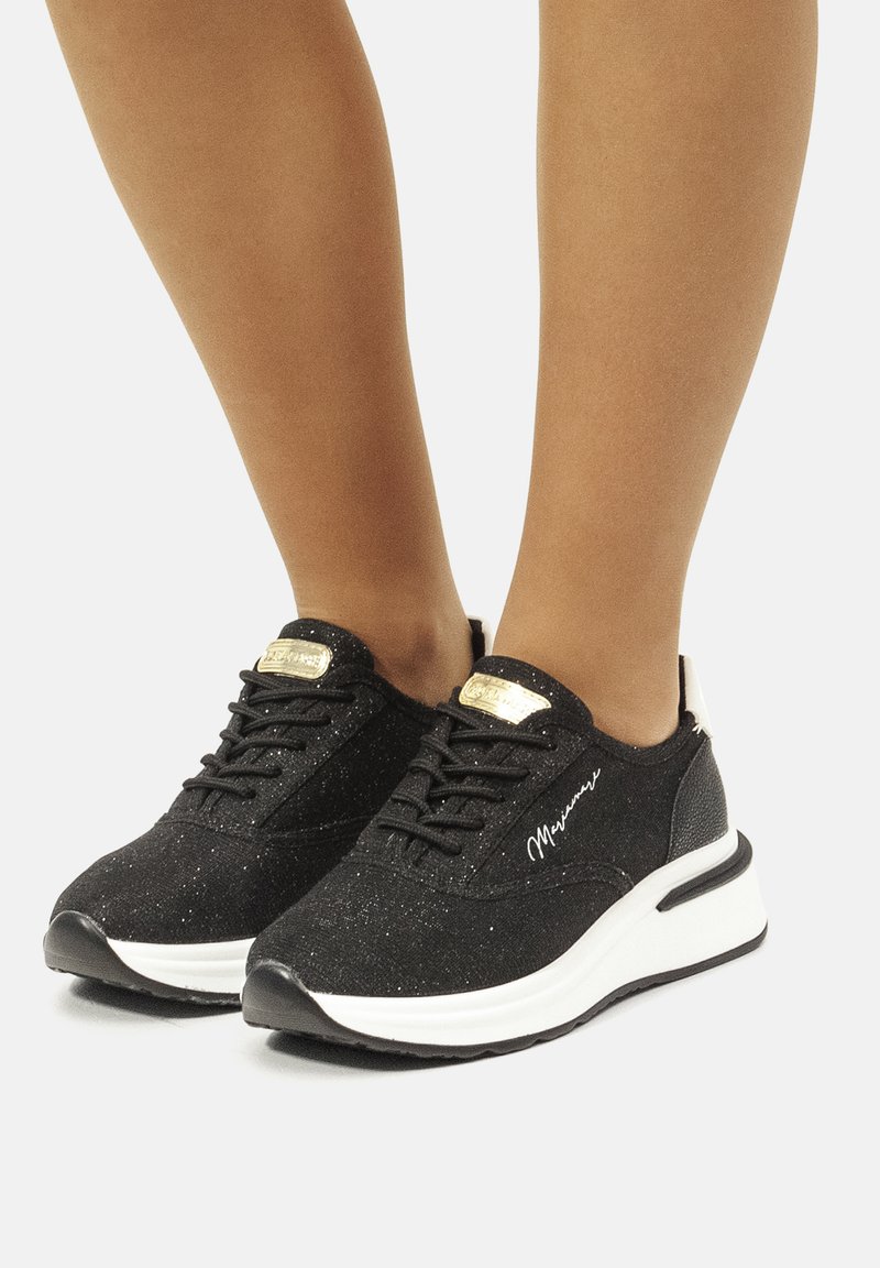 Schwarze Sportschuhe mit strukturierten Oberflächen, weißer Sohle, Schnürdesign und goldenen Akzenten. Enthält ein signatur Detail an der Seite.
