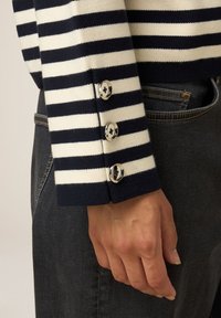 Pulover în dungi alb-negru, cu manșete șifonate, având trei nasturi argintii cu design floral. Purtați cu blugi negri.