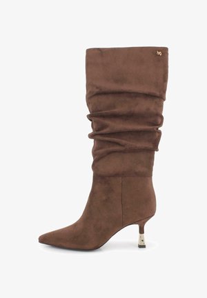 Bota de ante marrón hasta la rodilla con un diseño arrugado, puntera afilada y un tacón esbelto que presenta un acento metálico en la base del tacón.