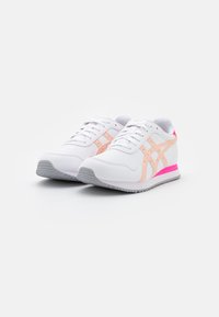 Vita atletiska skor med rosa och persikofärgade accenter, med en slät yta, snörningsdesign och strukturerad gummiyttersula.