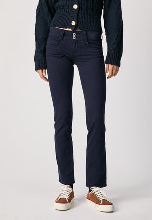 Jeans ajustados de color azul oscuro, fabricados con denim elástico, que cuentan con una cintura de altura media, dos bolsillos frontales y dos cierres de botón en la cintura.
