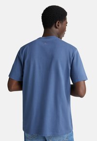 Modré bavlněné tričko s krátkým rukávem, kulatým výstřihem a jemným logem na zádech. Hladký materiál a klasický střih.