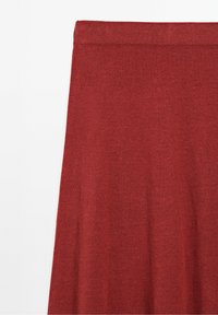 Jupe en tissu tricoté rouge avec une ceinture droite sur un fond clair uni.