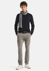 Námořnický svetr, světle šedé kalhoty a žebrovaný šedý šátek. Boty jsou bílé s hnědým reynolorum. Model stojí s rukama v kapsách.