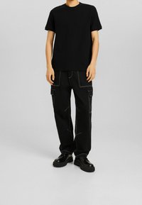 Black cotton t-shirt with short sleeves and crew neckline, paired with loose-fitting black cargo pants featuring white stitching and side pockets.