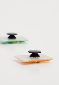 Two square silicone suction cup pads in green and orange with black knobs on top; translucent materials with smooth texture.