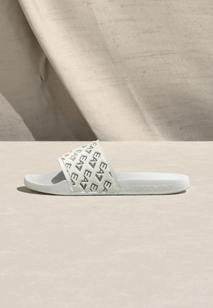 Bílá nazouvací sandála s širokým, texturovaným páskem zdobeným opakujícím se vzorem loga. Hladká gumová podrážka, minimalistický design, vhodná pro běžné nošení.