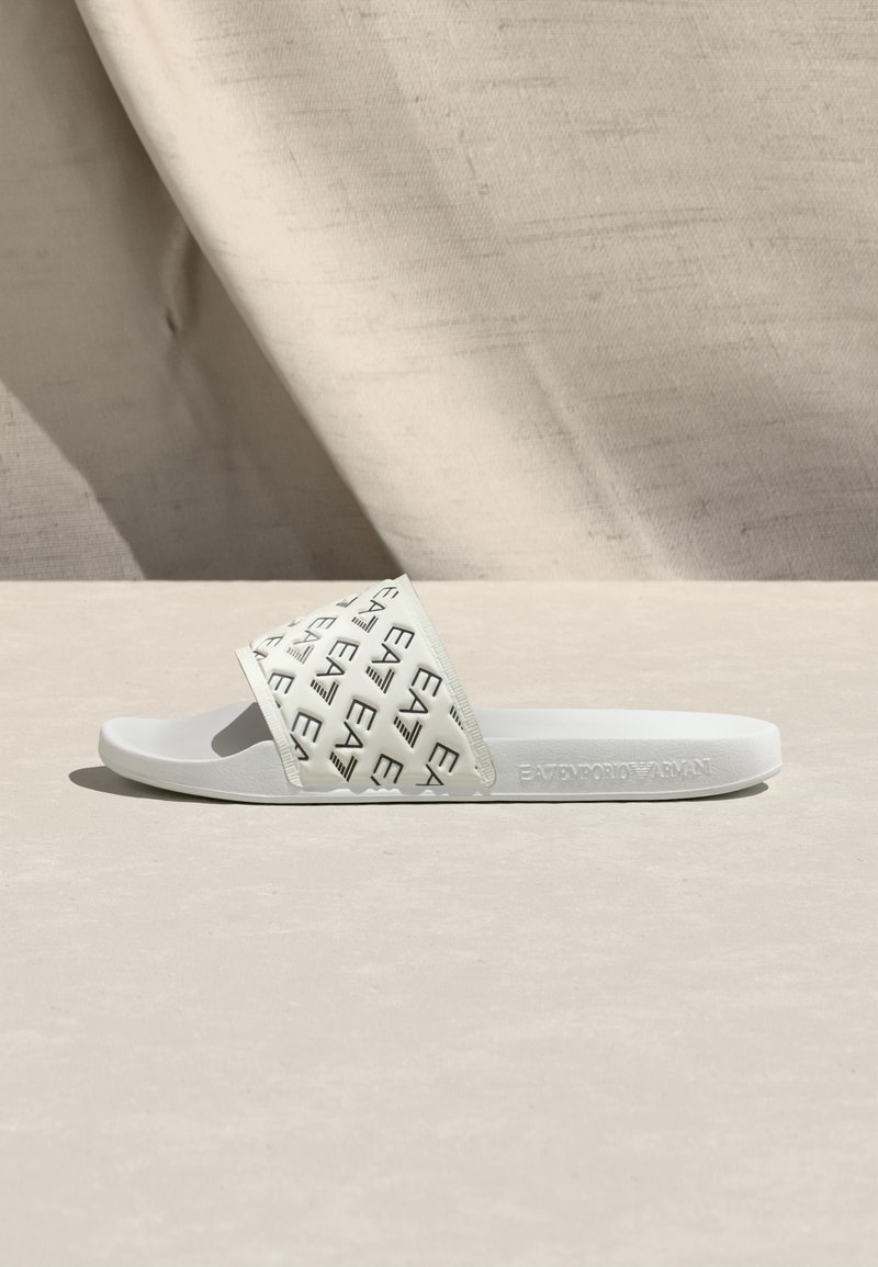 Λευκό σανδάλι με φαρδιά, υφασμένη λουρίδα που διαθέτει επαναλαμβανόμενο μοτίβο λογότυπου. Μαλακή σόλα από καουτσούκ, μινιμαλιστικός σχεδιασμός, κατάλληλο για καθημερινή χρήση.