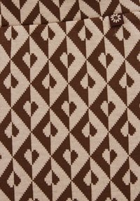 Brun och beige stickad tyg med ett diamantmönster som har hjärtan inuti varje diamant. Noterbar blomaccent nära toppen.