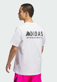 Hvid bomulds t-shirt med et stort sort prikket "ADIDAS" logo og "BASKETBALL" tekst på ryggen. Kortærmet og rundhalset design.
