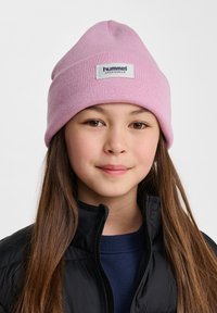 Rosa stickad mössa med en uppvikt kant; har ett inbroderat märke med texten "hummel sportswear." Bärs med en svart pufferjacka och en blå topp.