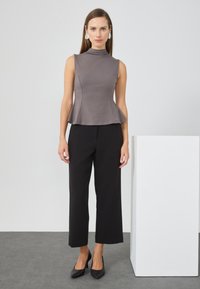 Grijze mouwloze top met een hoge hals en uitlopende zoom, gecombineerd met zwarte wijde broek en zwarte hoge hakken. Gladde stofstructuur.
