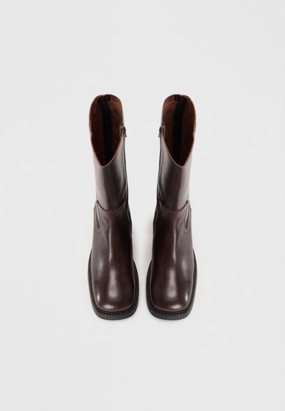 Brown leather ankle boots with side zippers, pointed toes, and a smooth finish. Includes decorative stitching along the edges.