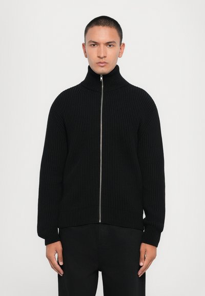 Maglione nero a costine con zip, colletto alto e maniche lunghe. Presenta una zip argentata, vestibilità rilassata e tessuto testurizzato.