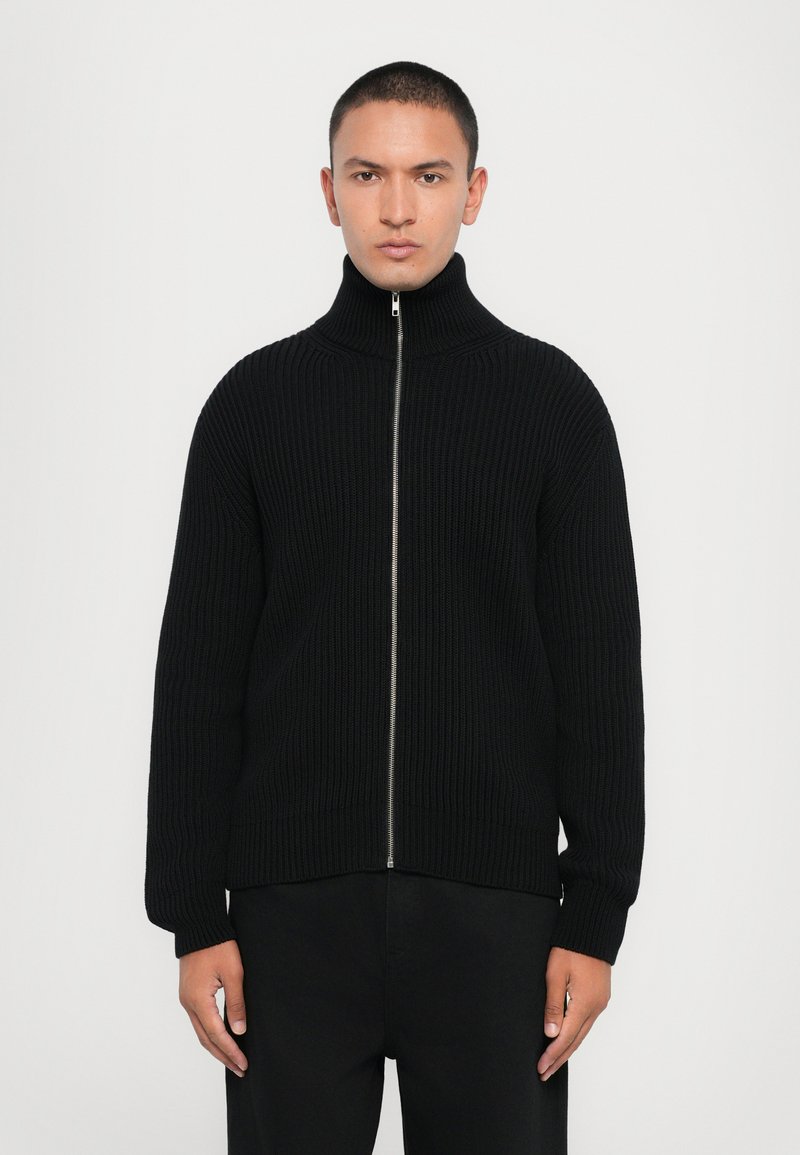 Black ribbed knit zip-up sweater with a high collar and long sleeves. Features a silver zipper, relaxed fit, and textured fabric.