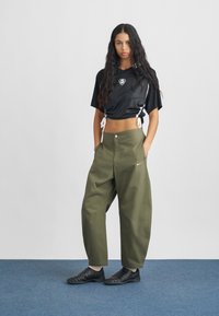 Svart croppad tröja i jersey med mesh-textur och sidoband, kombinerad med lösa olivgröna byxor med knäppning och framfickor.