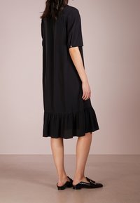 Vestido negro de longitud a la rodilla con un ajuste relajado, mangas cortas y un dobladillo con volantes. La tela parece suave y ligera.
