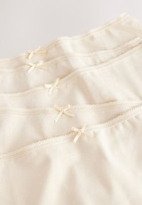 Stack of five cream-colored cotton underwear with lace trim and small decorative bows along the waistband.
